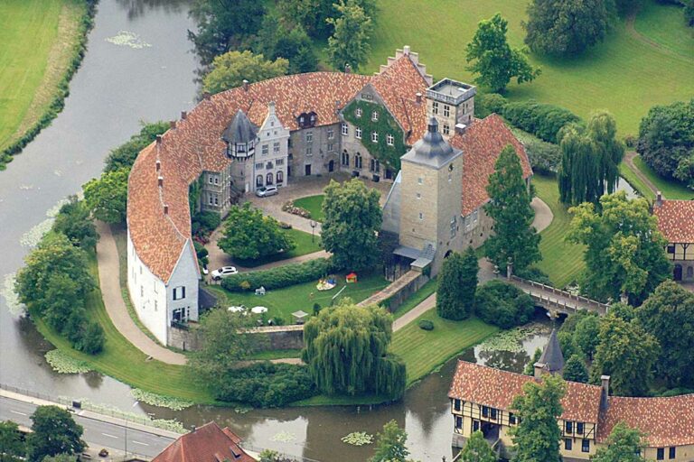 Luftaufnahme des Schlosses Burgsteinfurt, umgeben von einem Wassergraben und grüner Landschaft.
